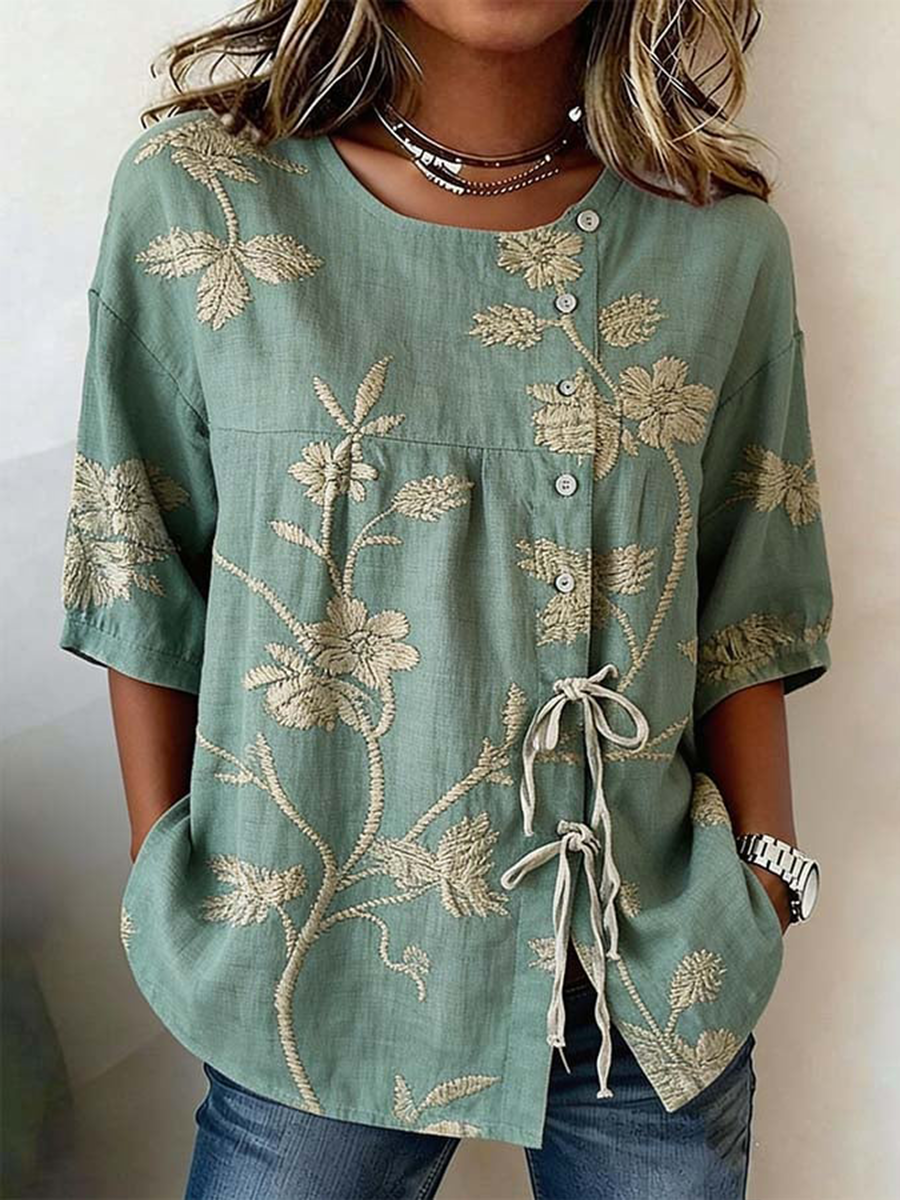 Damebluse i linnedblanding med knapper og snører, prydet med planter og blomster