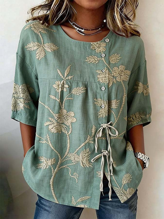 Damebluse i linnedblanding med knapper og snører, prydet med planter og blomster